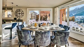 A dining area with a large table set for six, surrounded by blue chairs, with a view of a snowy landscape through large windows. - Chalet D'Espoir - Pure Alpine Luxury! (Montriond)