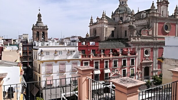 A view of a historic building with ornate architecture, including domes and spires, and a balcony with a metal railing.