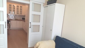 A living room with a blue sofa, a white wardrobe, and a kitchen in the background.