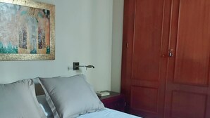 A bedroom with a bed, pillows, a nightstand, a lamp, a wooden wardrobe, and a painting on the wall.