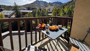 Un balcón con una mesa dispuesta para el desayuno, con vistas a un paisaje montañoso y edificios al fondo.