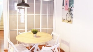 Una mesa redonda de madera con cuatro sillas blancas, una planta pequeña en maceta y una lámpara colgante negra.