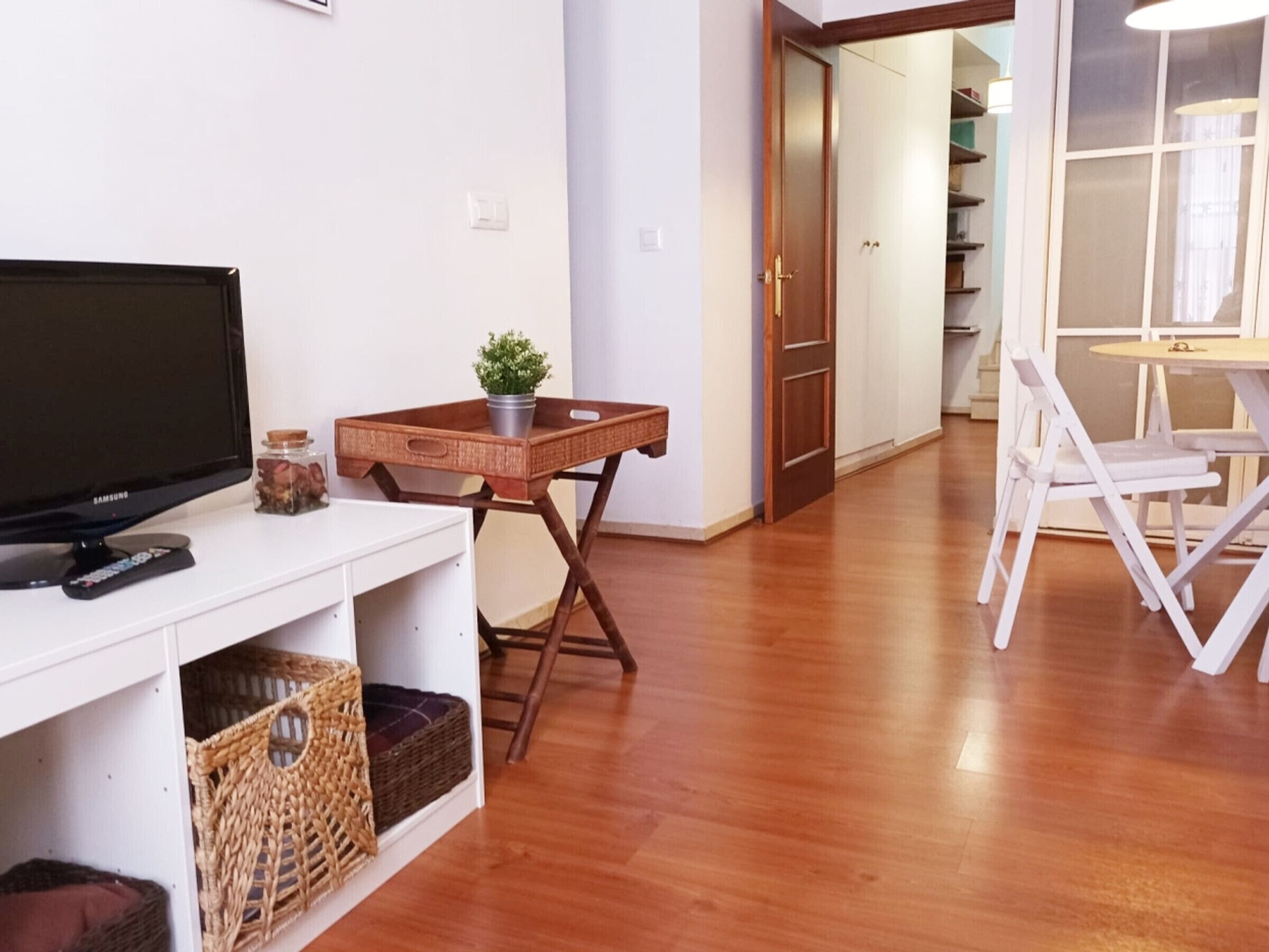 Un soggiorno con televisore, un tavolino con una pianta, cesti in vimini e pavimento in legno.