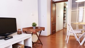 Una sala de estar con televisor, una mesita con una planta, cestas de mimbre y suelo de madera.