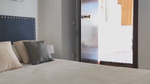 Un dormitorio con cama, almohadas, cabecera, una puerta y vistas al exterior.