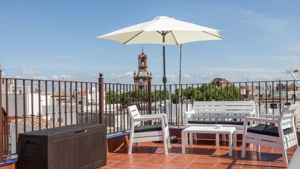 A rooftop terrace with a white umbrella, white lounge chairs, and a black heater. - Beautiful apartment in Seville's historic center (Sevilla)