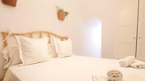 A neatly made bed with white linens and pillows, a rolled towel on the bed, and a small plant on the wall. - Beautiful apartment in Seville's historic center (Sevilla)