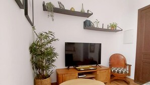 A living room with a TV, wooden furniture, a potted plant, and wall-mounted shelves. - Beautiful apartment in Seville's historic center (Sevilla)