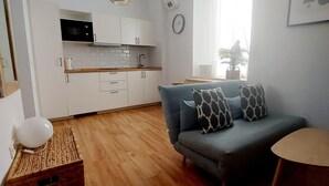 A modern kitchen with white cabinets, a microwave, and a sink. There is a blue sofa with patterned cushions and a small round table. - Beautiful apartment in Seville's historic center (Sevilla)