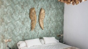 Une chambre à coucher avec un lit, deux décorations murales en forme d’ailes, une lampe de chevet et une petite table ronde.