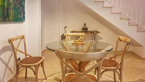 Un coin repas avec une table en verre et quatre chaises en bois. Une statue est posée sur la table, et un escalier se trouve à l’arrière-plan.