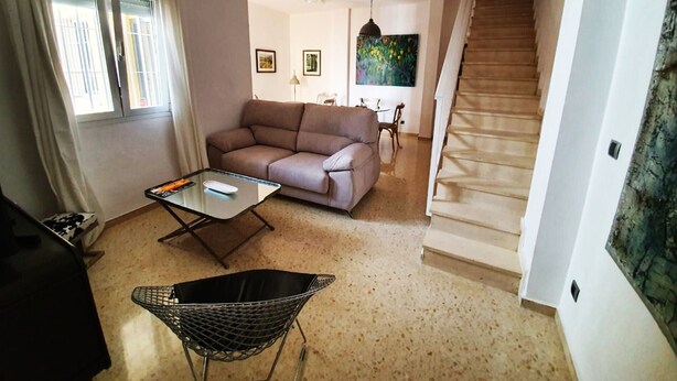 Un salon comprenant un canapé, une table basse, un luminaire suspendu et un escalier menant à un autre niveau.