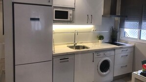 Cocina compacta con microondas integrado, lavamanos de acero inoxidable y lavadora de carga frontal.