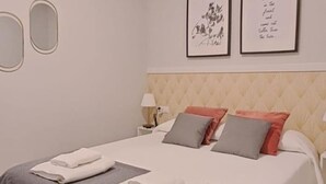 Una cama bien hecha con almohadas y toallas dobladas, una lámpara de noche y cuadros en la pared.