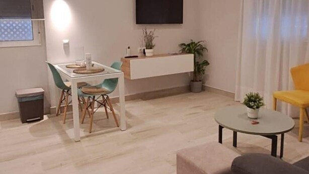 Una sala de estar moderna con comedor, televisor de pantalla plana en la pared y una mesita con planta en maceta.