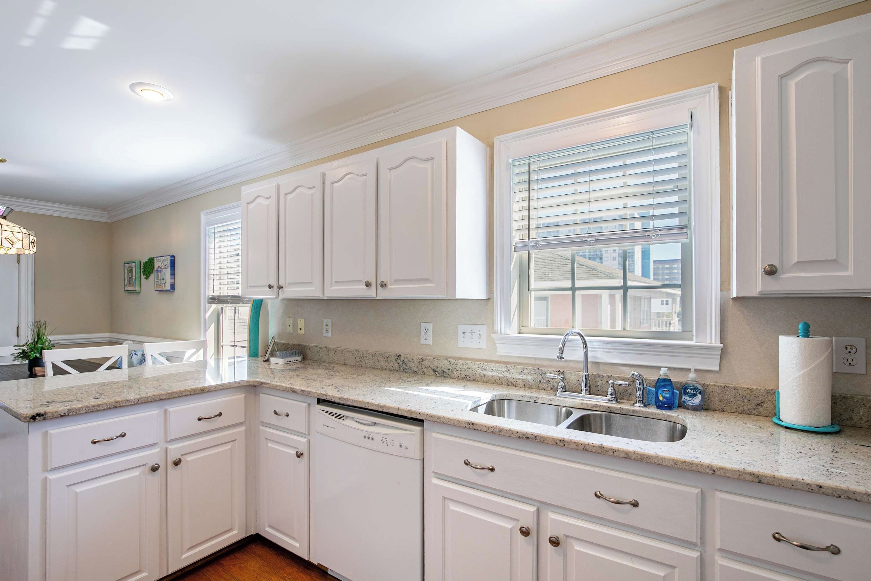 A kitchen with white cabinets, a granite countertop, a dishwasher, and a window with blinds.