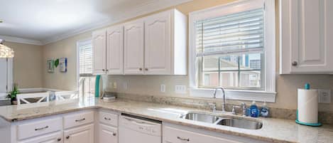 A kitchen with white cabinets, a granite countertop, a dishwasher, and a window with blinds.