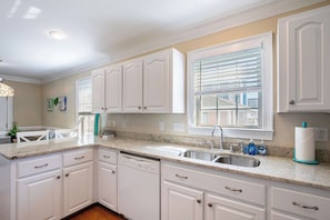 A kitchen with white cabinets, a granite countertop, a dishwasher, and a window with blinds.