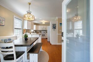 A modern kitchen with white cabinetry, a wooden dining table, and a hanging light fixture. - Spacious 3BR Getaway with BBQ, close to Beach (North Myrtle Beach)