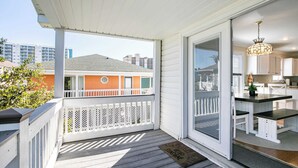 Ein überdachter Balkon mit weißer Geländer, eine Glasschiebetür zu einer Küche mit weißen Schränken und einer schwarzen Arbeitsplatte.