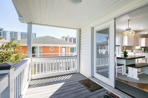 A covered porch with a white railing, a sliding glass door leading to a kitchen with white cabinets and a black countertop.