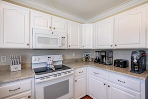 A kitchen with white cabinets, a microwave, a stove, and a coffee maker.
