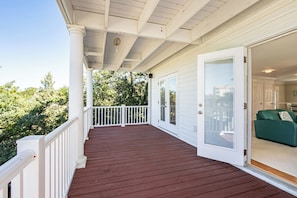 A covered porch with a red wooden floor, white railings, and a door leading to an interior room with a green sofa.