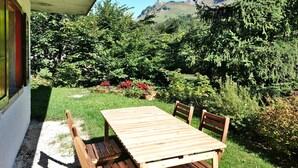 A wooden table and chairs set on a patio with a view of a mountainous landscape. - 6-person apartment in quiet chalet near slopes (Le Grand-Bornand)
