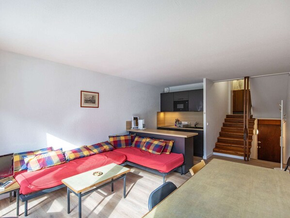 Un espacio habitable compacto con sofá, una mesita, kitchenette y una escalera.