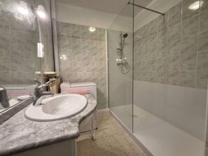 Une salle de bain dotée d’une douche à parois de verre, d’un lavabo avec un plan de toilette en marbre et de toilettes agrémentées d’une serviette rose.