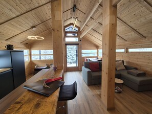 A wooden cabin interior with a dining area, a sofa, and a kitchen.