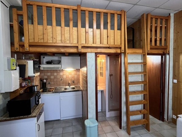 A compact kitchen with a built-in upper sleeping area, a sink, and a microwave.