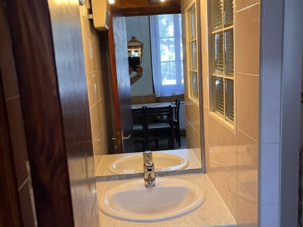 A bathroom with two sinks and a mirror reflecting a dining area with chairs and a table.
