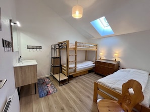 A room with bunk beds, a desk, a vanity, and a skylight.