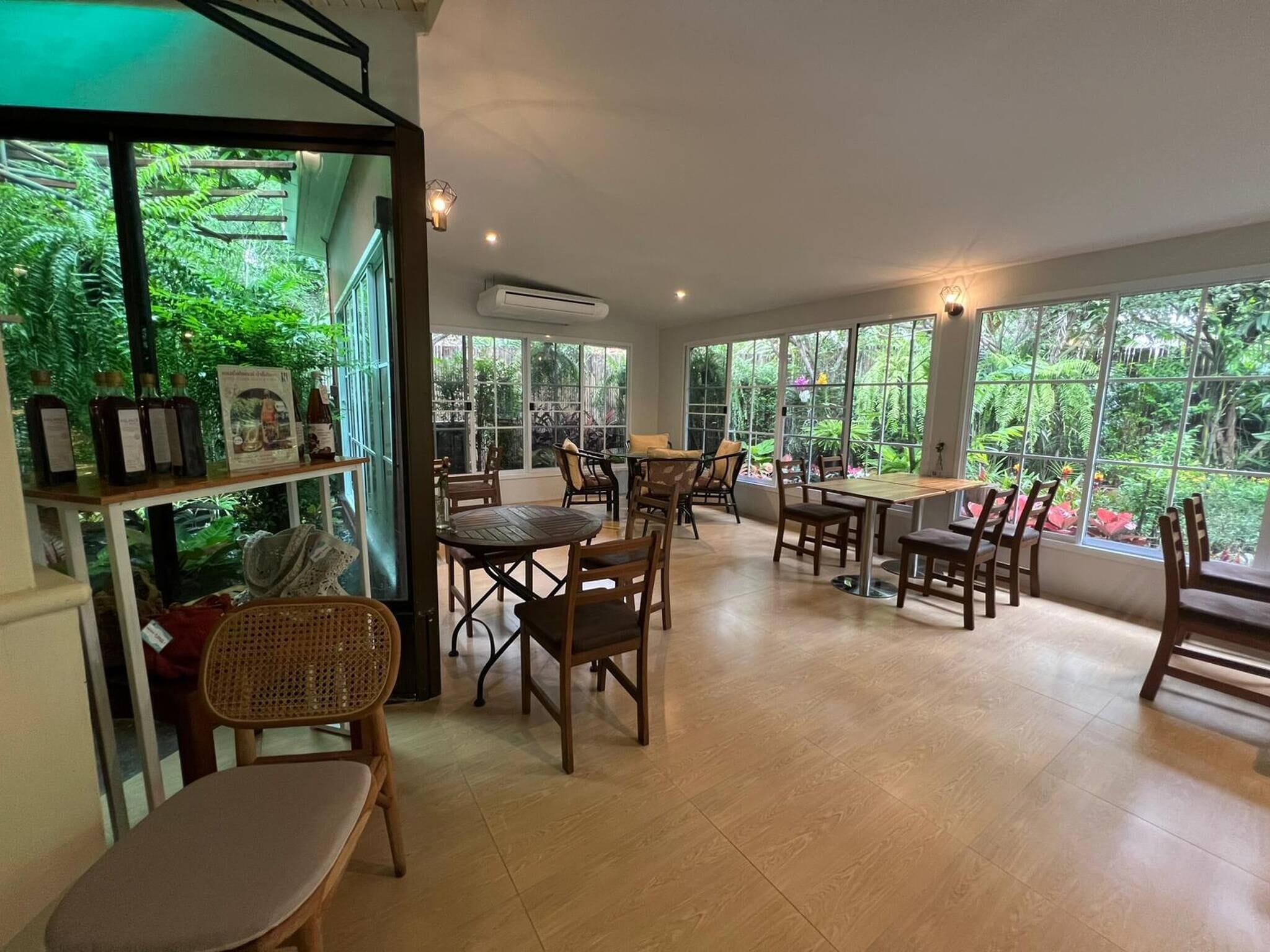 Un restaurante con vista a un jardín tropical, muebles de madera y un amplio ventanal.