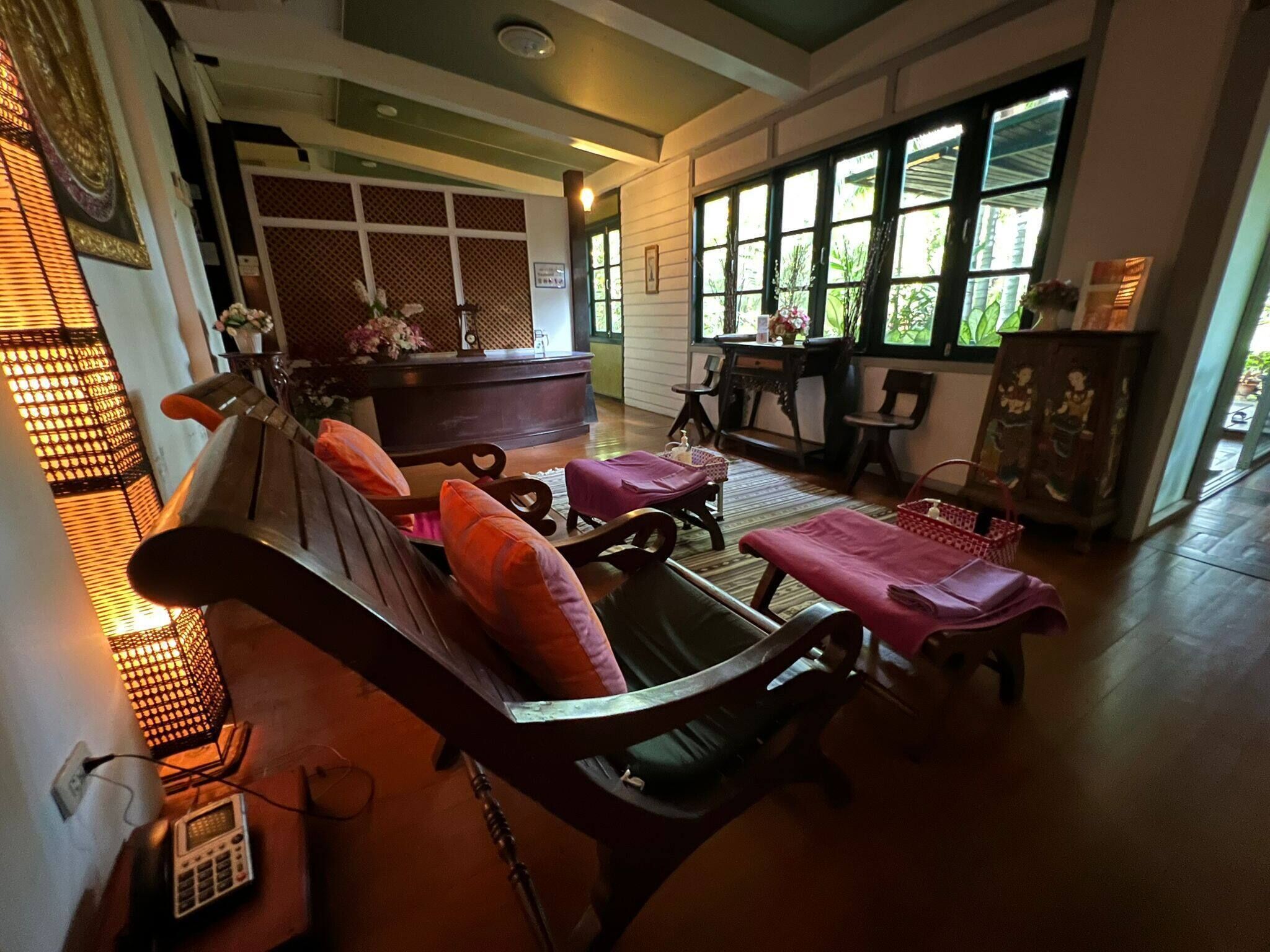 A traditional room with a wooden sofa, a small table, and a bench. There are windows with a view of greenery outside.