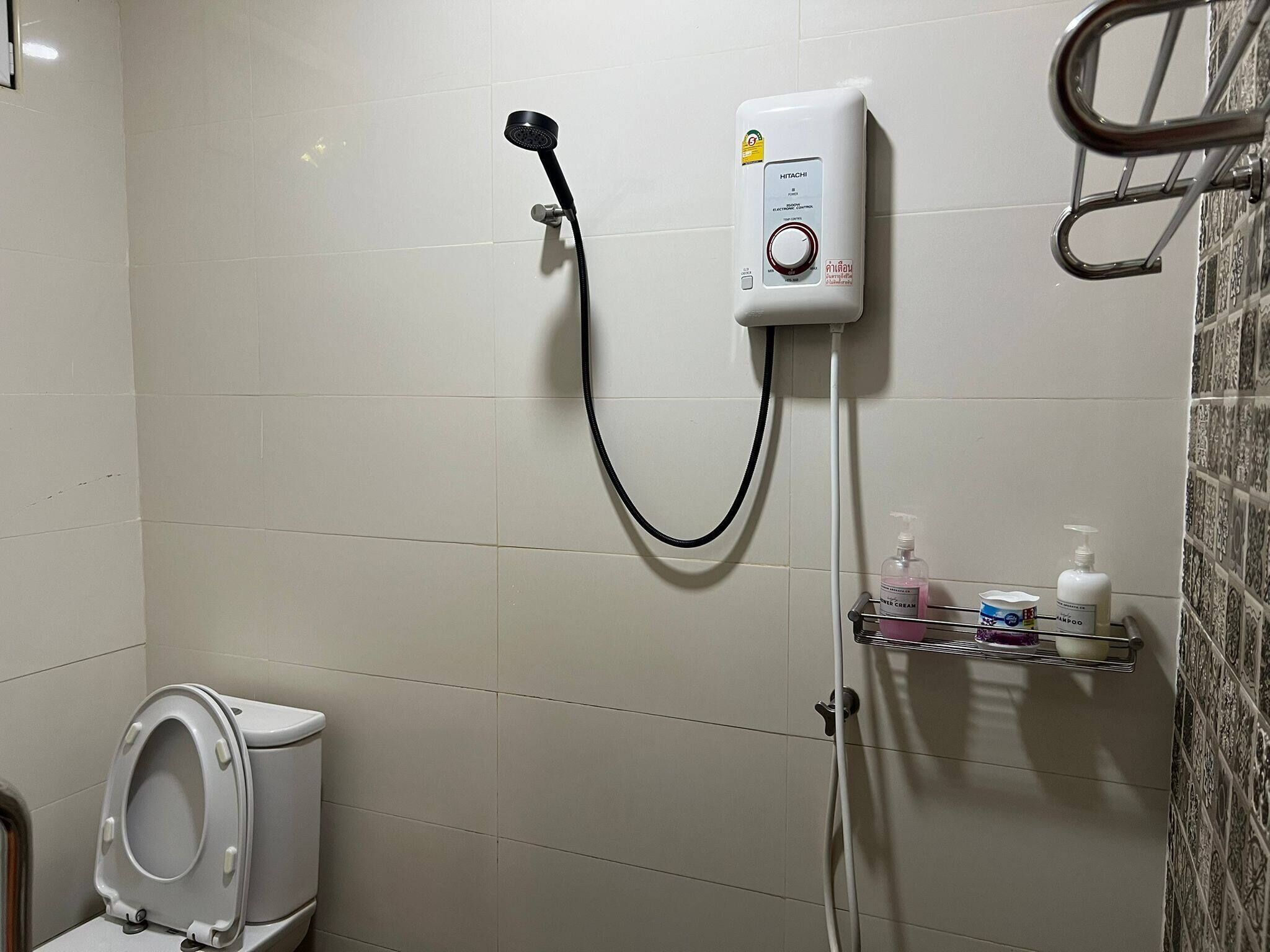 Une salle de bain avec des toilettes blanches, une douche dotée d’un panneau de commande et une étagère contenant des articles de toilette.