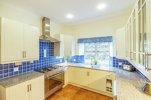 Una cocina con armarios blancos, una campana extractora de acero inoxidable, un backsplash de azulejos azules, una ventana con cortinilla azul y una encimera de granito.