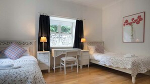 Een slaapkamer met twee bedden, een bureau en een stoel, met een raam en een lijst met een afbeelding aan de muur.