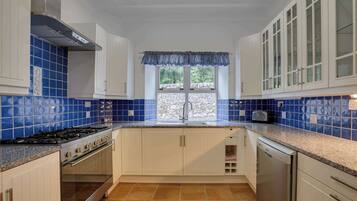 A kitchen with blue-tiled backsplash, white cabinets, a stainless steel range hood, a built-in oven, and a dishwasher.