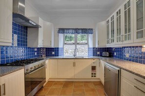 Una cocina con salpicadero de azulejos azules, armarios blancos, una campana extractora de acero inoxidable, un horno empotrado y un lavavajillas.