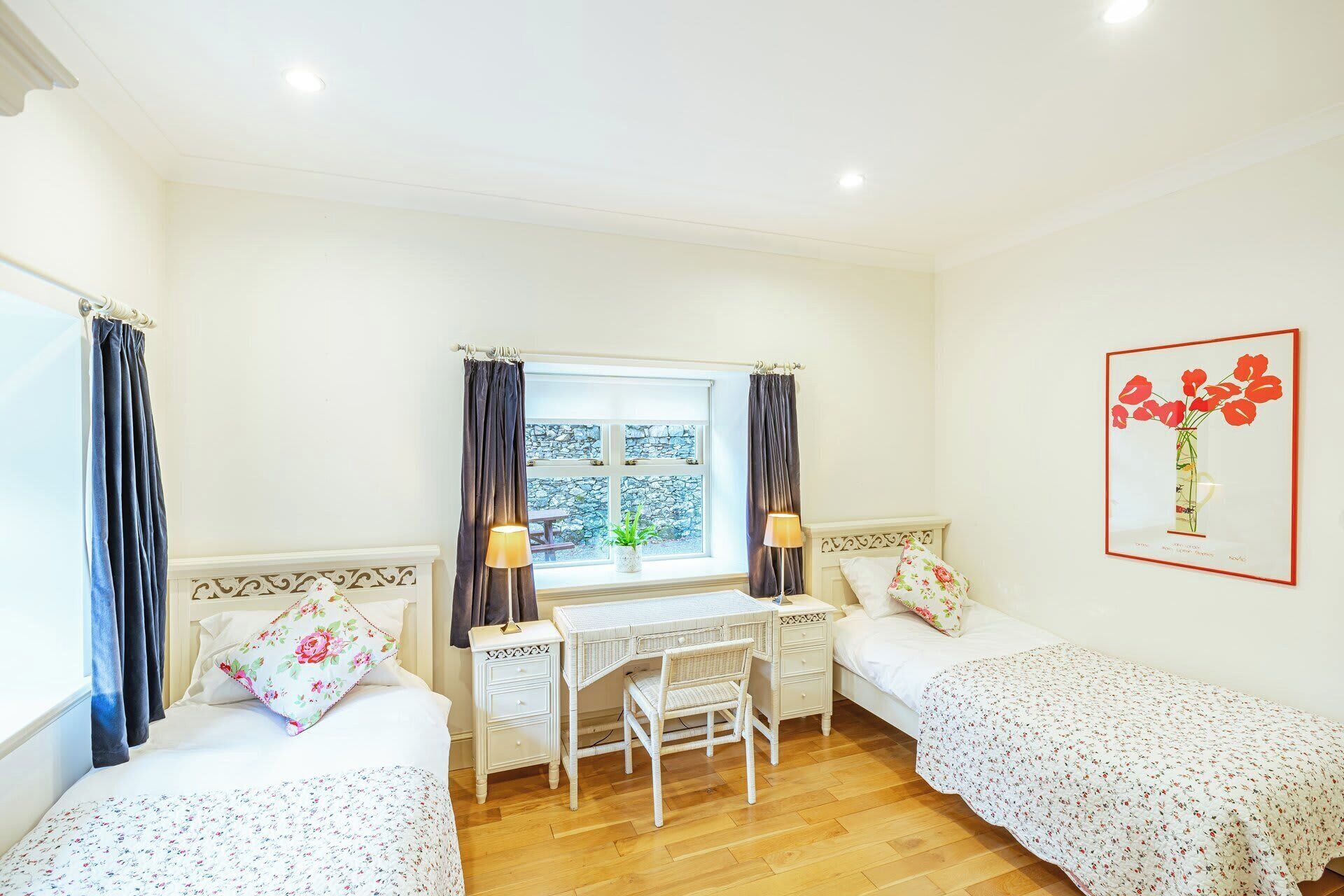 A room with two single beds, a desk with a chair, and a window with curtains.