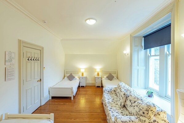 Un dormitorio con dos camas individuales, un sofá, un ventanal con vistas y una puerta con perchero.