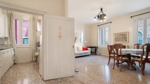 A room with a dining table, chairs, a sofa, a radiator, and a window with a view. - Biennale Apartment 'A Short Walk' (Venezia)