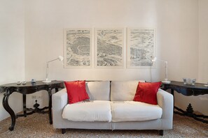 Une pièce avec un canapé blanc, deux coussins rouges, une table noire et trois œuvres d’art encadrées accrochées au mur.