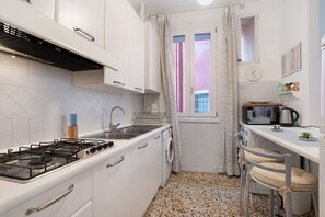 Une cuisine de taille réduite équipée d’une cuisinière à gaz, d’un évier et d’un lave-linge.