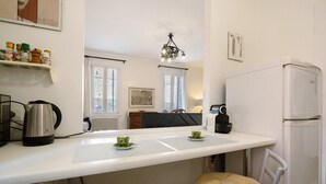 A compact kitchen with a white countertop, a kettle, a refrigerator, and a dining area with a chair and a table. - Biennale Apartment 'A Short Walk' (Venezia)