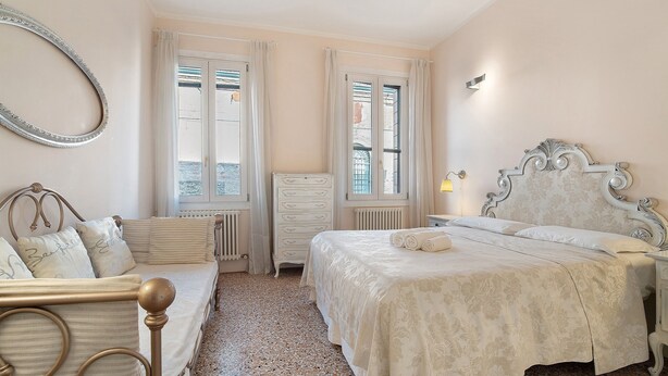 A bedroom with a bed, a bedside table, a dresser, a radiator, and a window with curtains. - Biennale Apartment 'A Short Walk' (Venezia)