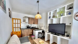 A modern kitchen with a microwave, stove, and sink. There is a wooden dining table with a bowl. A TV is mounted on a white shelf. - Apartment 'Rey Melchor' with Mountain View, Private Terrace and Wi-Fi (Trevélez)
