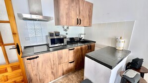 A compact kitchen with wooden cabinets, a stainless steel range hood, a microwave, and a sink. - Apartment 'Rey Melchor' with Mountain View, Private Terrace and Wi-Fi (Trevélez)